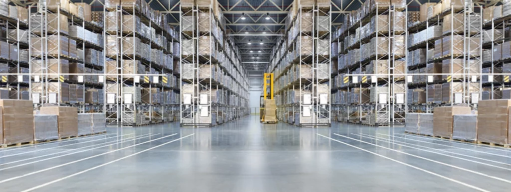 Image of the inside of a big warehouse with forklift, shelves, pallets, and boxes.